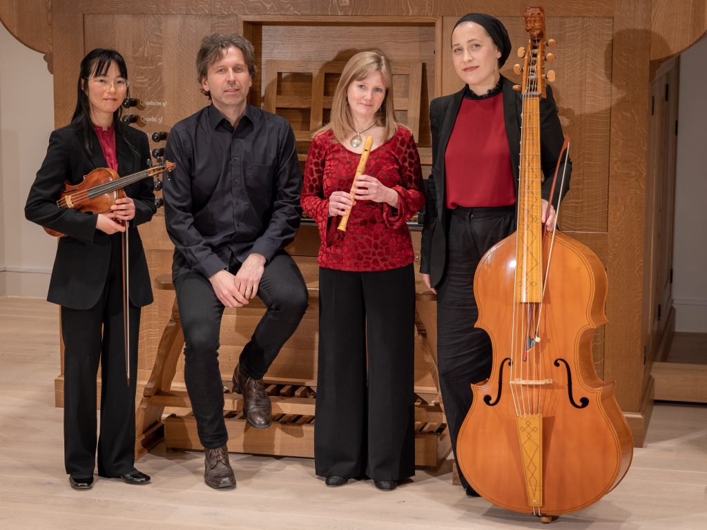 4 musicians with instruments next to pipe organ
